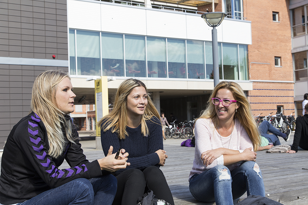 Tre kvinnor sitter framför en större byggnad.